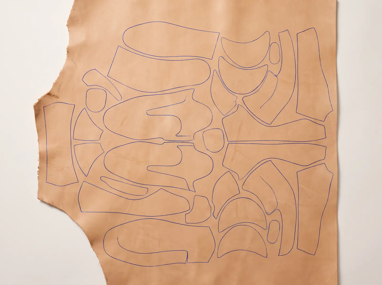 Shoe pattern pieces nested tightly on a leather hide, outlined in blue.